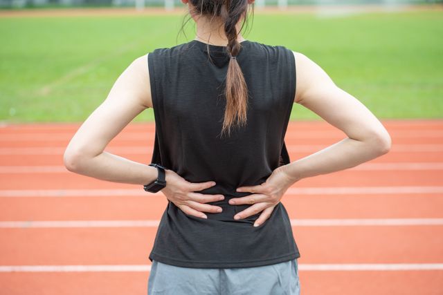 back view of young runner woman suffering from backache or sore waist after running in the running track in stadium