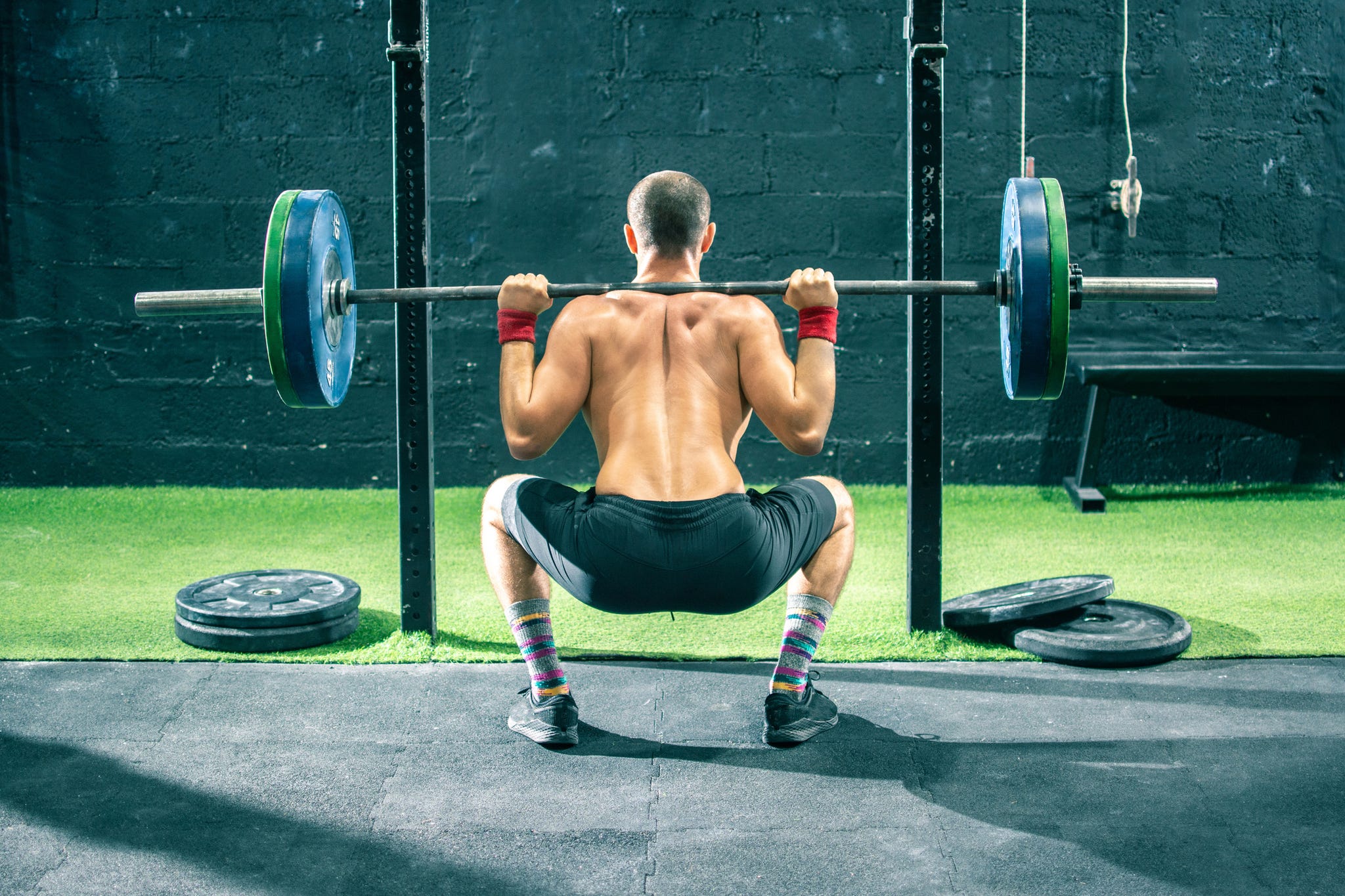 back view of young sportsman lifting a barbell at the gym