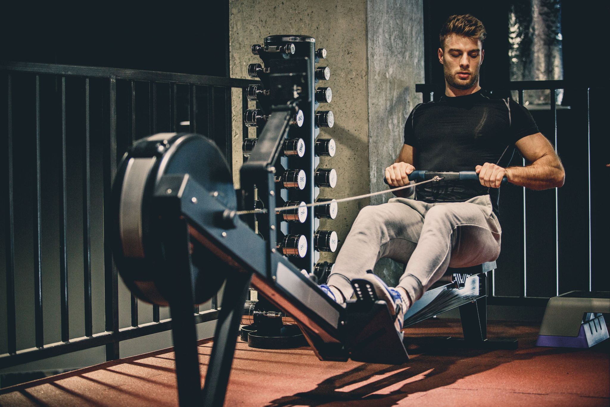 caucasian young man is using rowing machine for cardio training in the gym