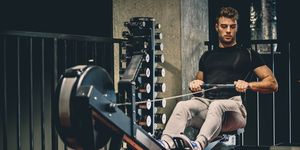 caucasian young man is using rowing machine for cardio training in the gym