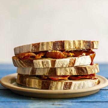 a close up side view of a bacon sandwich with brown sauce on a plate, placed on a wooden surface
