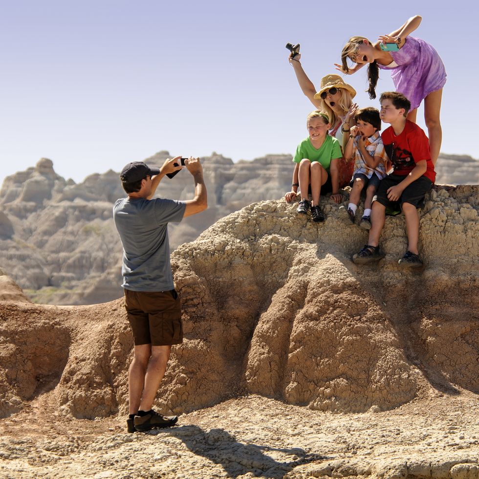 a family poses for a photo by a rock formation in badlands national park, a good housekeeping pick for best cheap places to travel