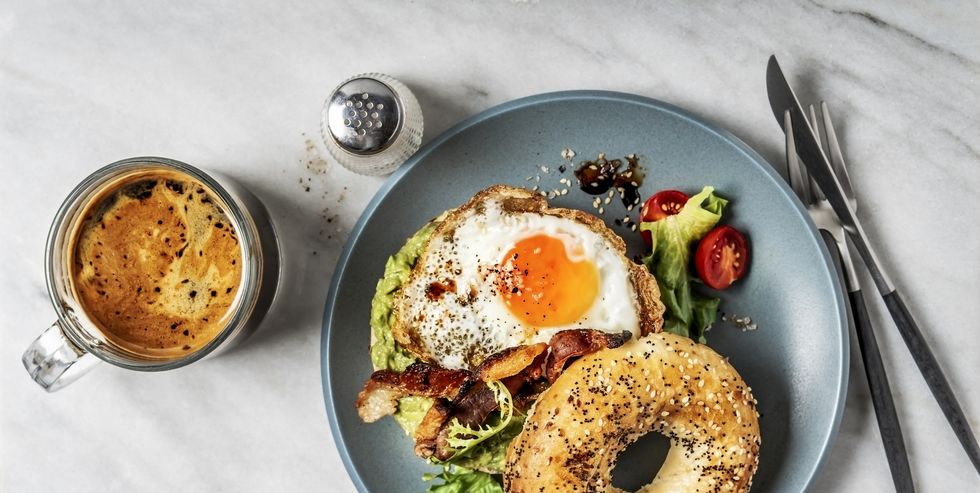 Bagel sandwich with avocado, fried egg and side salad on white background