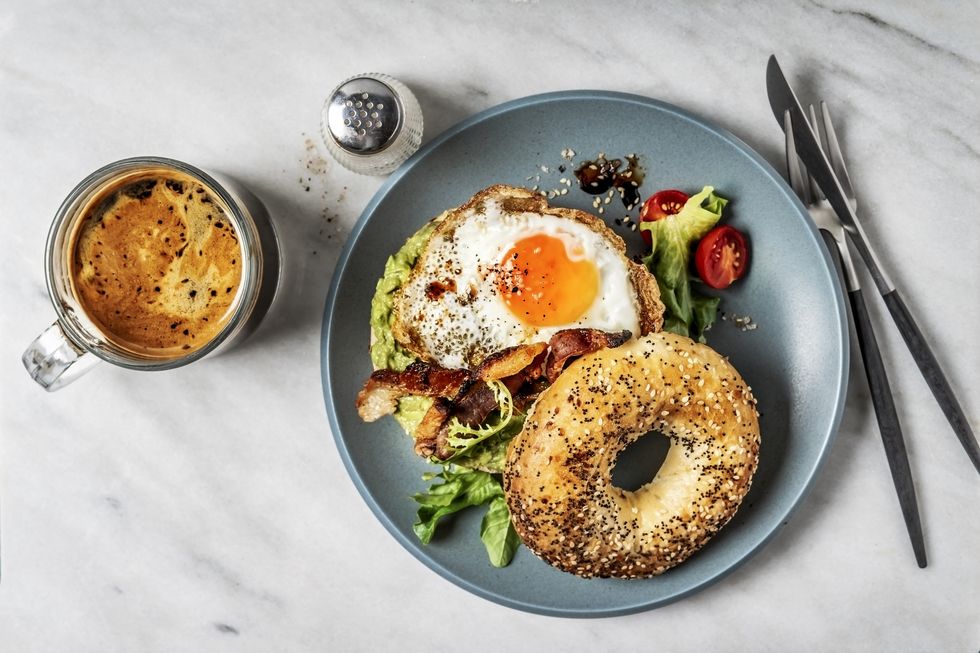 bagel sandwich with avocado, fried egg and side salad on white background