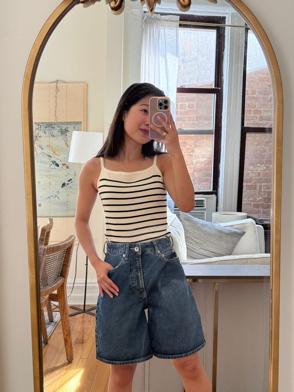 a person wearing a striped tank top and denim shorts posing in front of a mirror