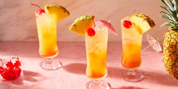 orange cocktail in a glass with ice with cherries and a pineapple wedge