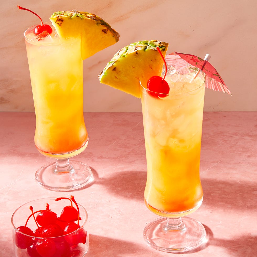 orange cocktail in a glass with ice with cherries and a pineapple wedge