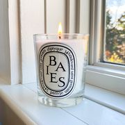 lit baies diptyque candle on window sill