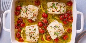 baked cod in a dish with lemon wedges and burst tomatoes