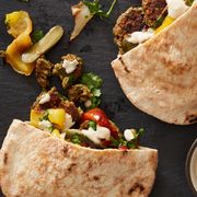 roasted vegetables and baked falafel with tahini sauce spilling out of pitas on a black slate background