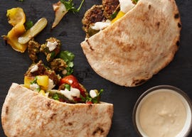 roasted vegetables and baked falafel with tahini sauce spilling out of pitas on a black slate background