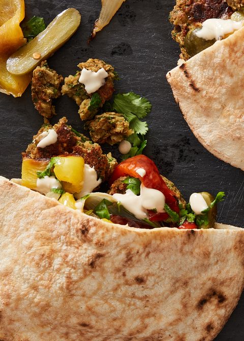 roasted vegetables and baked falafel with tahini sauce spilling out of a pita on a black slate background
