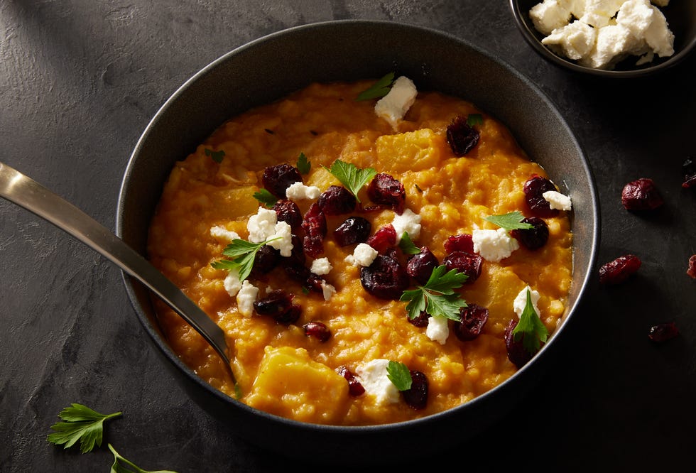baked pumpkin risotto in a black bowl topped with cheese and dried cranberries