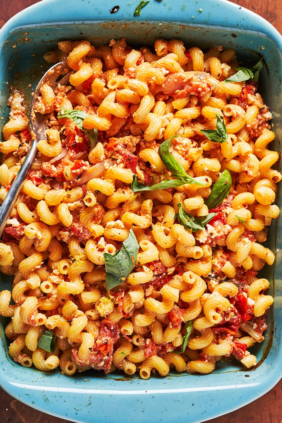 baked feta pasta garnished with basil in a teal baking dish