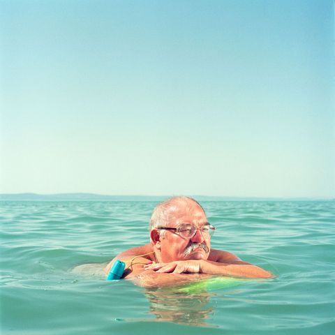 Met een ouderwets plastic strandbeursje om de arm dobbert een man in het Balatonmeer