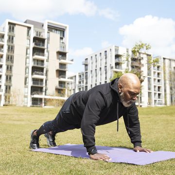 bald man doing push ups on exercise mat at park