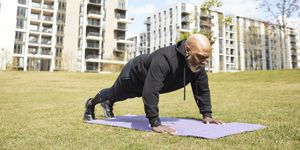 bald man doing push ups on exercise mat at park