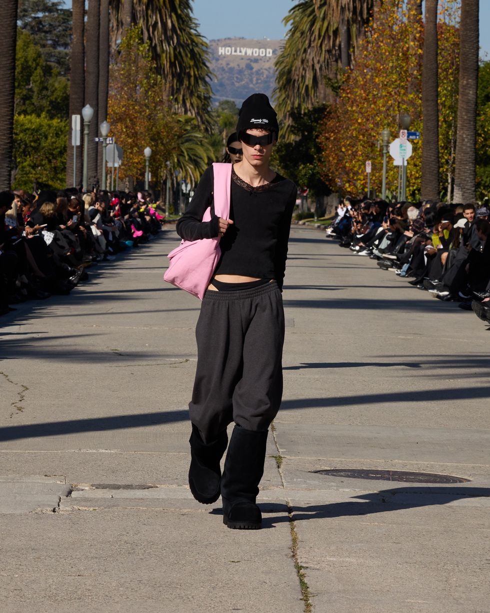 a person in a black hat and sunglasses walking down a street