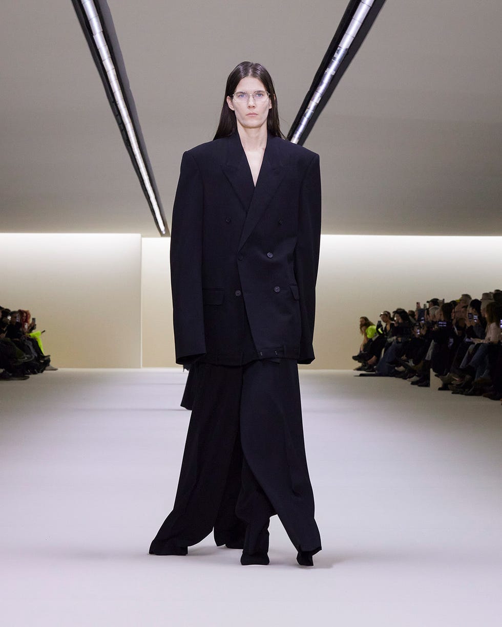 A model walks the Balenciaga Fall 2023 runway in an oversized black coat with black tailored pants.