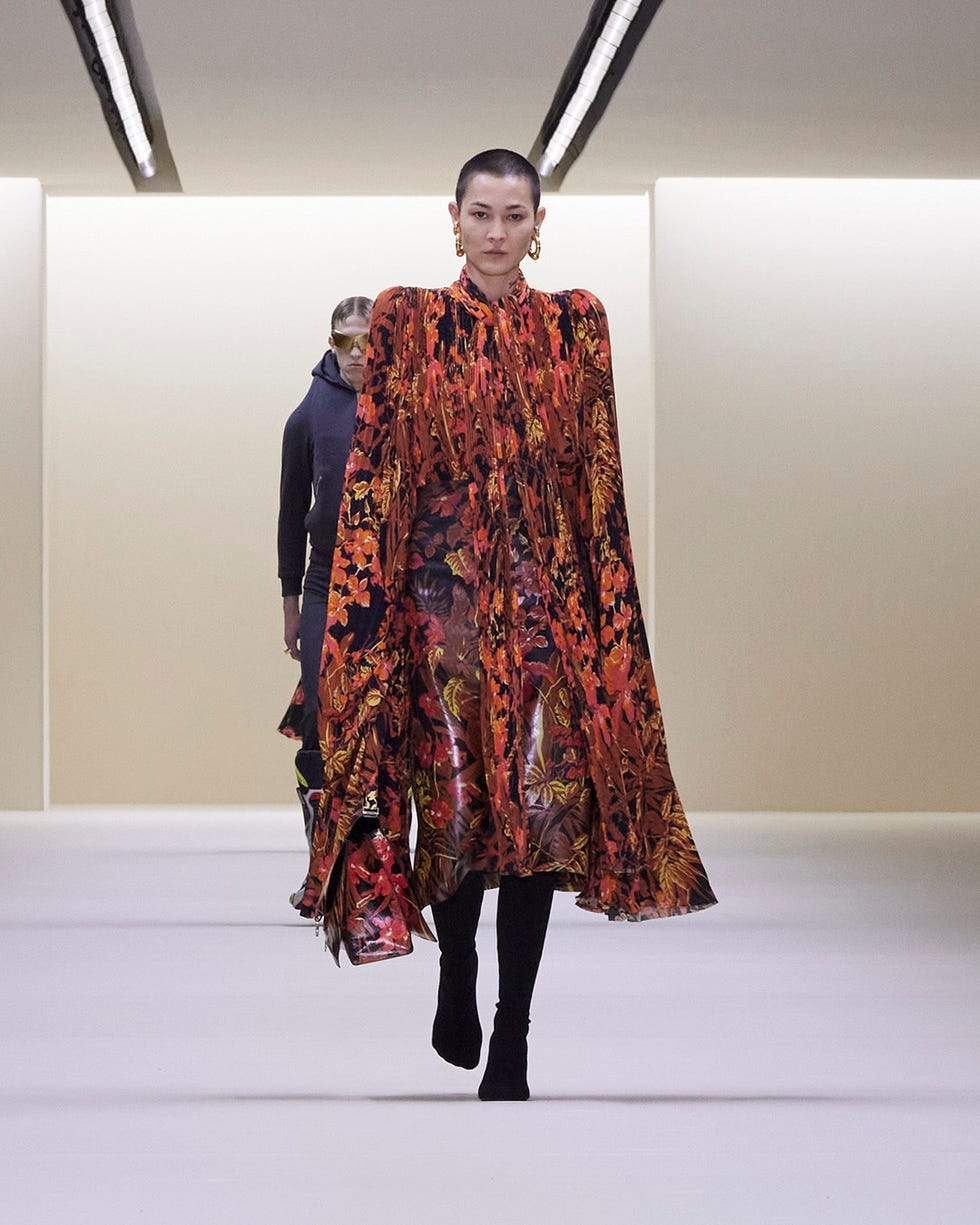 A model walks the runway in a red and gold floral print dress with rounded shoulders at the Balenciaga Fall 2023 show.