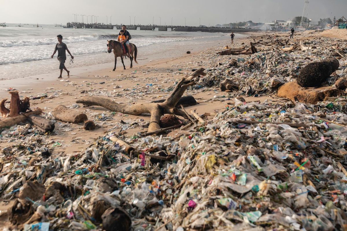 Toeristen rijden op 27 januari 2019 op een paard over Kedonganan Beach op Bali Tijdens het regenseizoen van november tot maart spoelen duizenden kilos afval aan op de stranden Daarom wordt het ook wel plasticseizoen genoemd