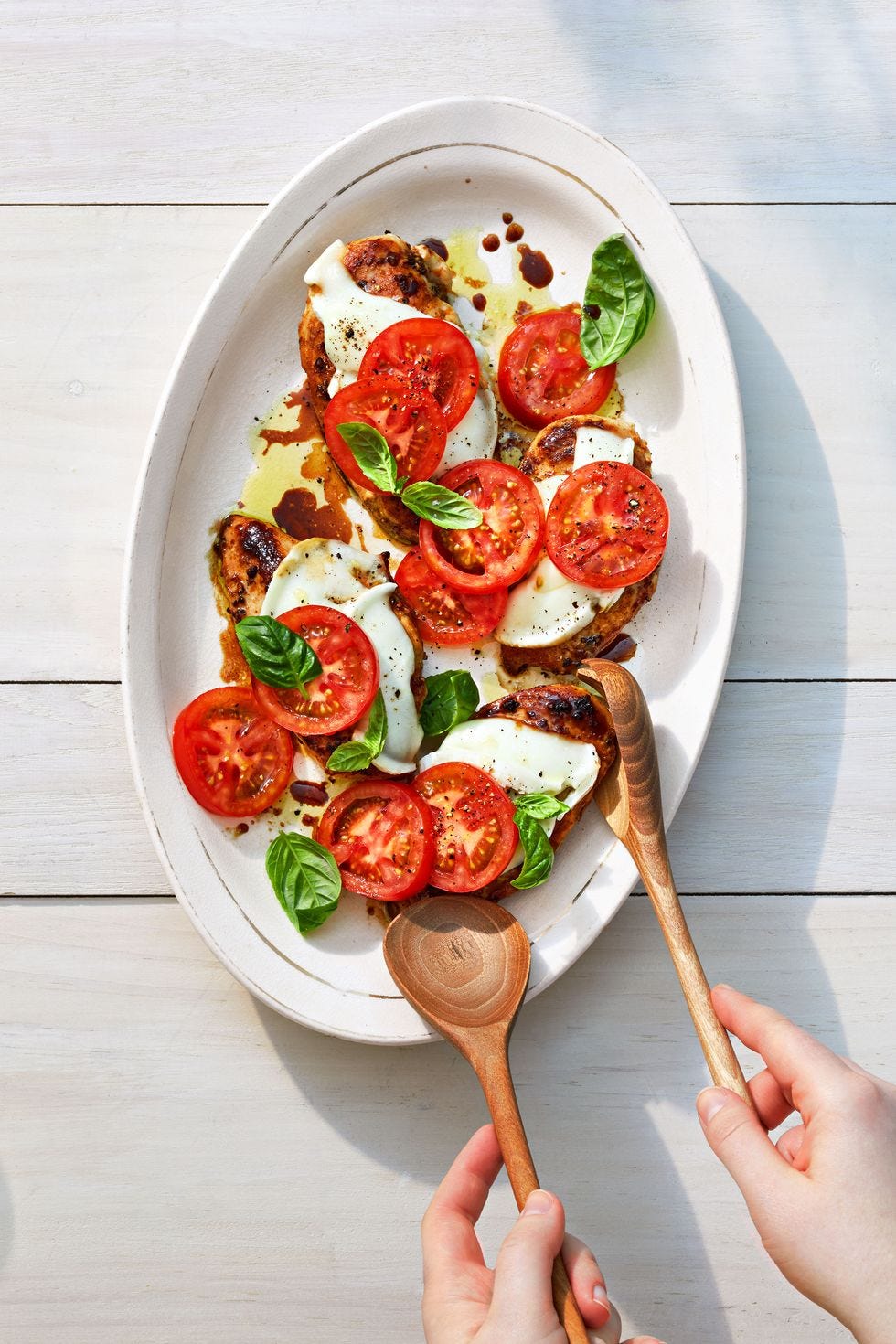 a platter of grilled chicken topped with melted mozzarella, sliced tomatoes and basil