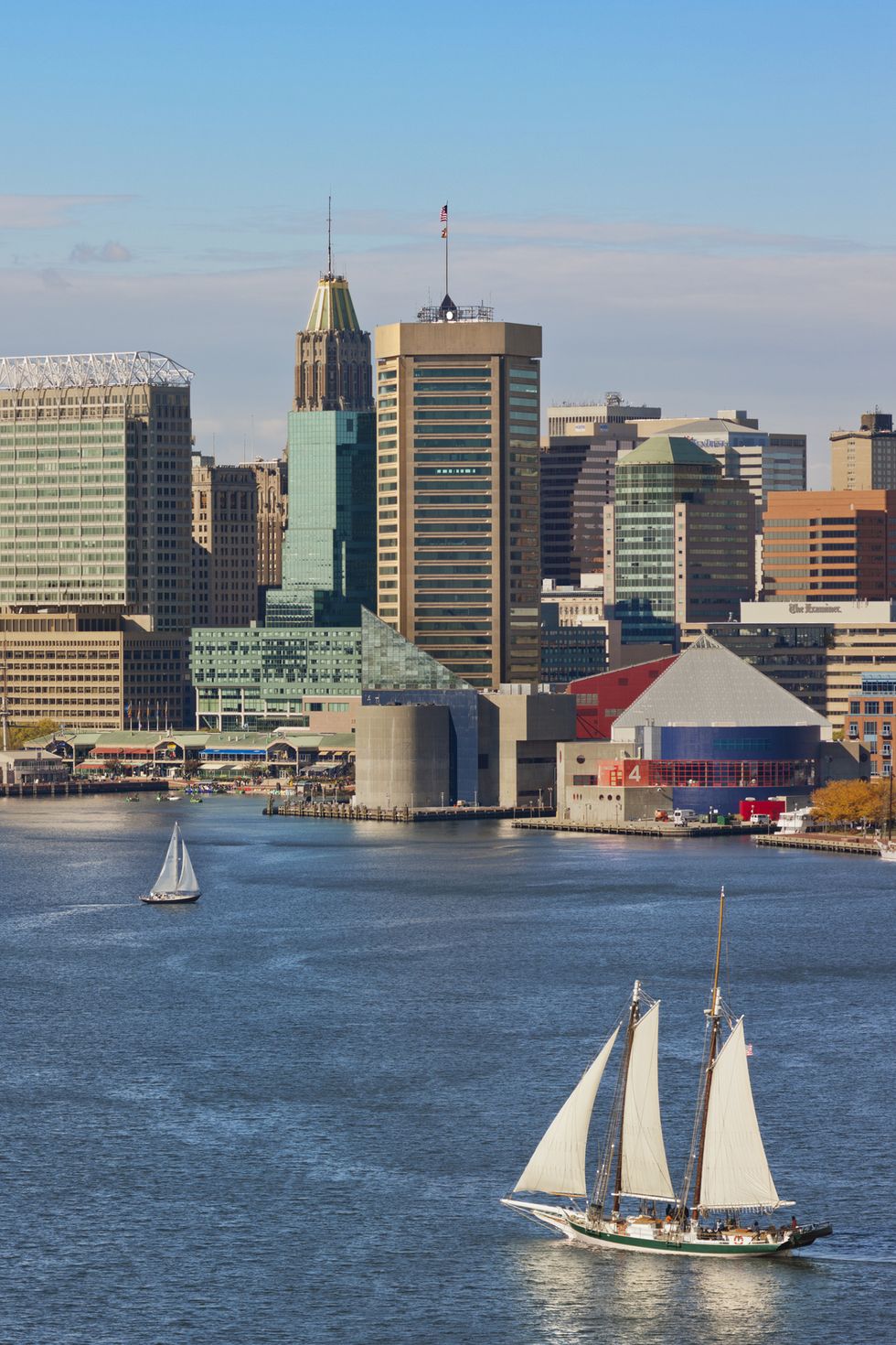 baltimore skyline and inner harbor with three sail boat on the water in foreground and two sail boat in background