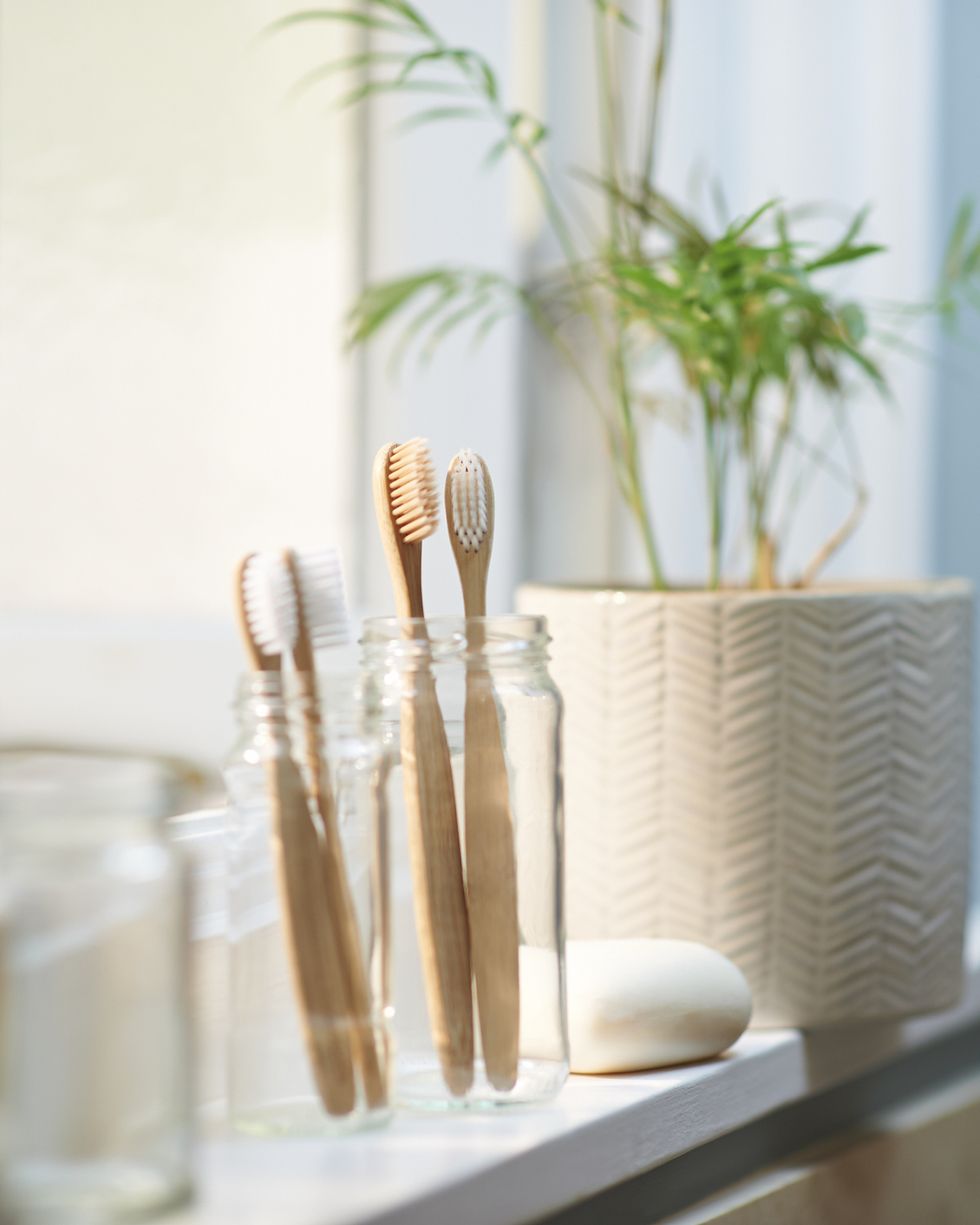 plastic free wooden family toothbrushes in a glass jar along side other zero waste products on a bathroom window sill