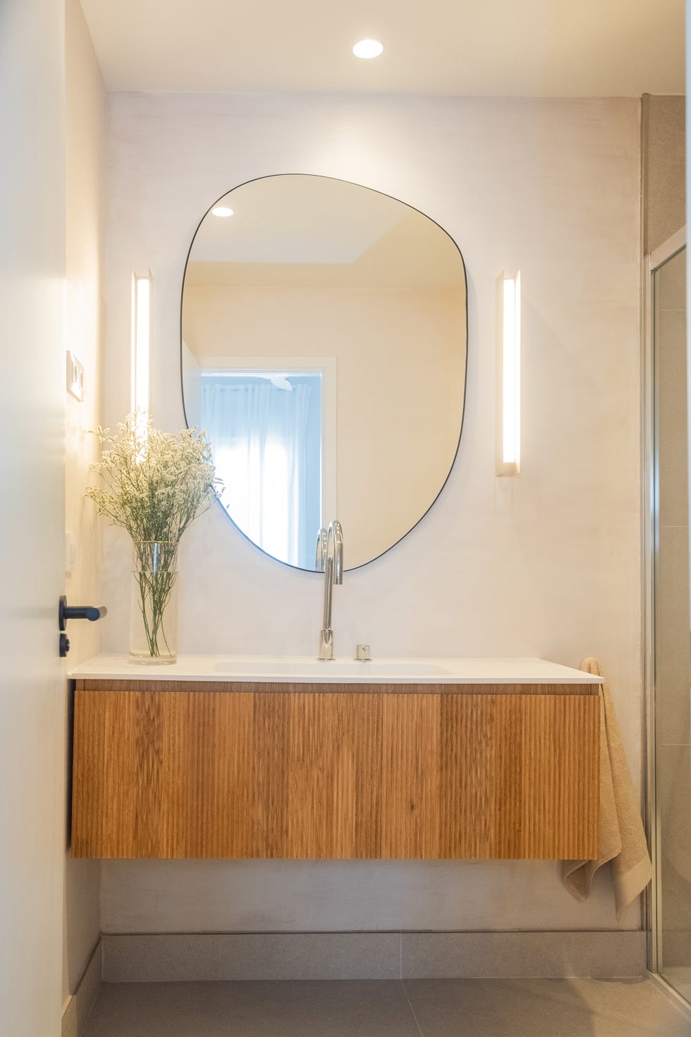 mueble de baño volado con frente de palillería y espejo con forma orgánica