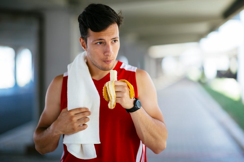 young athletic man eating banana and resting after workout in the city street.
