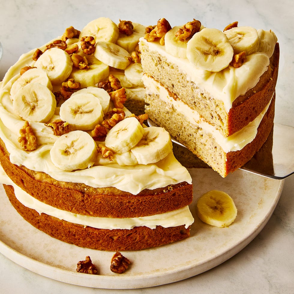 layered cake with cream cheese frosting topped with banana slices and walnuts