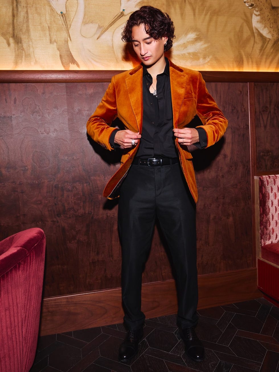 person wearing an orange velvet blazer and black pants posing in a restaurant setting