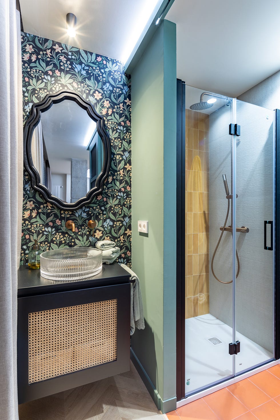 mueble de baño negro volado con frente de rejilla, papel pintado con motivos florales y cabina de ducha con azulejos en color mostaza