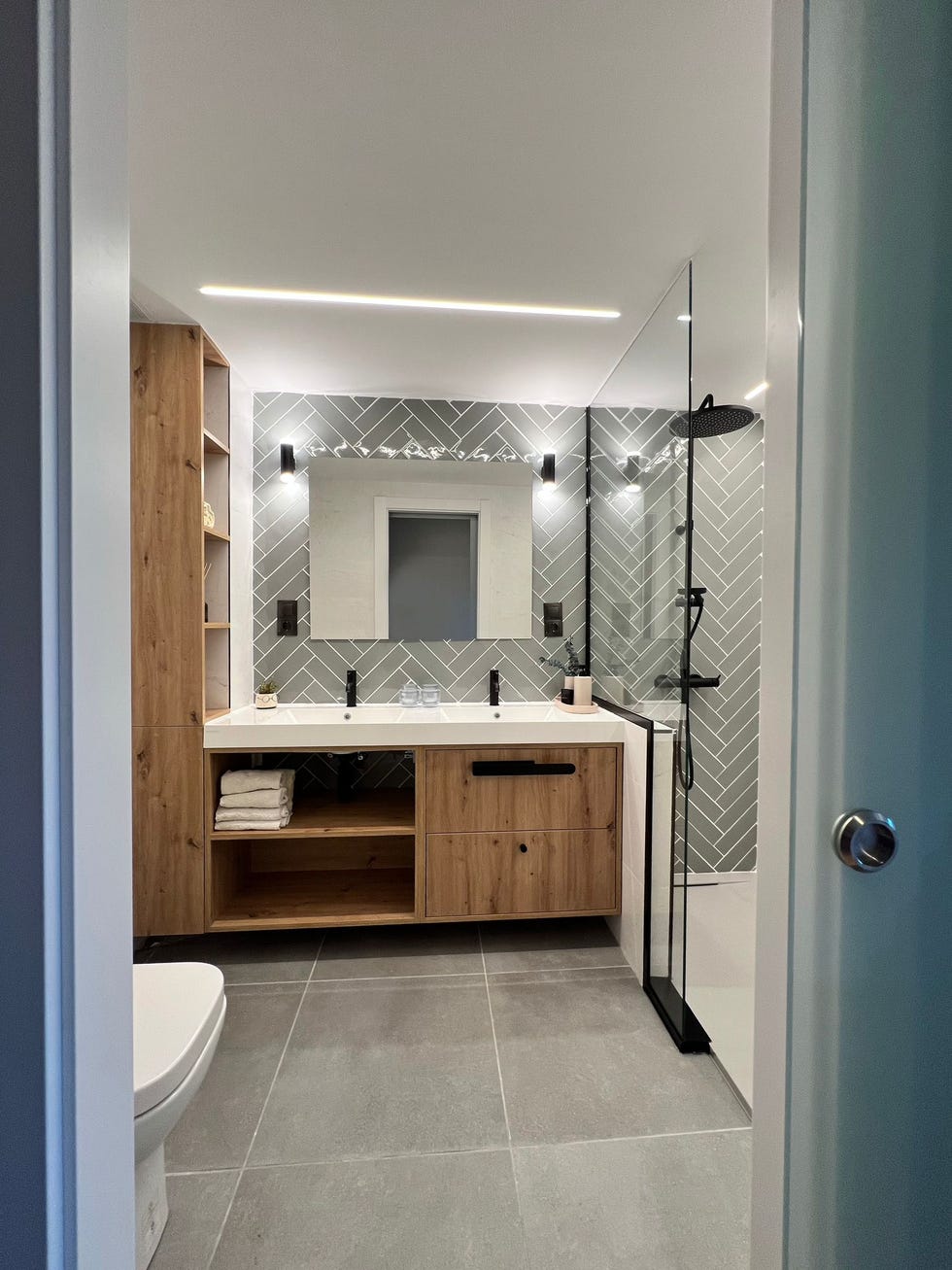 mueble de lavabo de madera y frente de azulejos en espiga que se extienden hasta la ducha