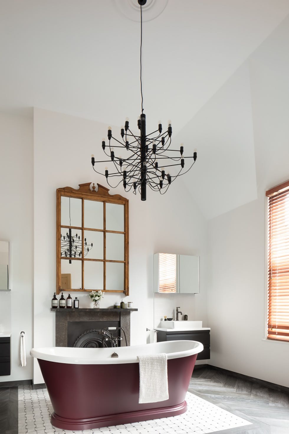 baño de estilo clásico con bañera exenta color vino, chimenea de piedra y lámpara de techo de araña
