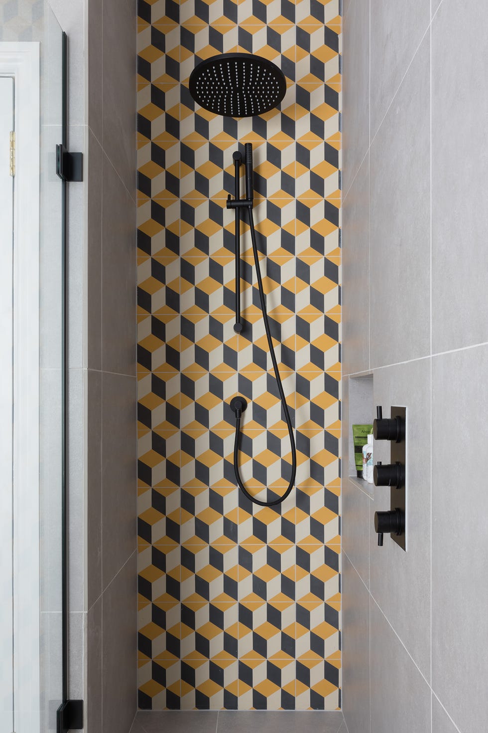 ducha de obra con pared de azulejos con mosaicos geométricos y grifería en negro mate