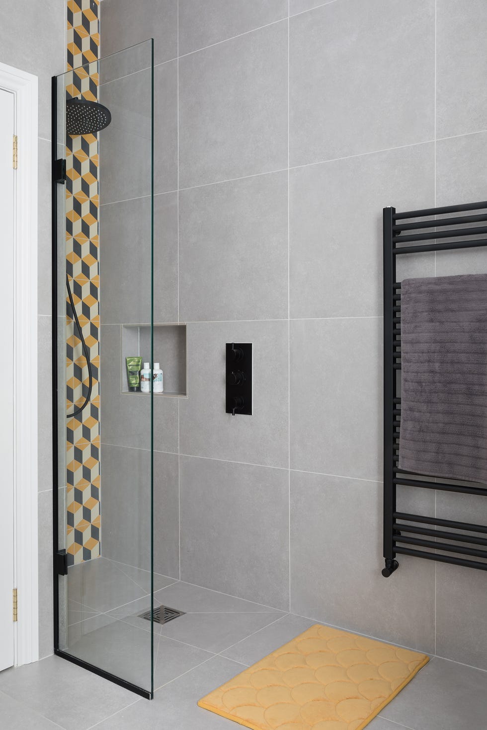 ducha de obra con pared de azulejos con mosaicos geométricos y grifería en negro mate