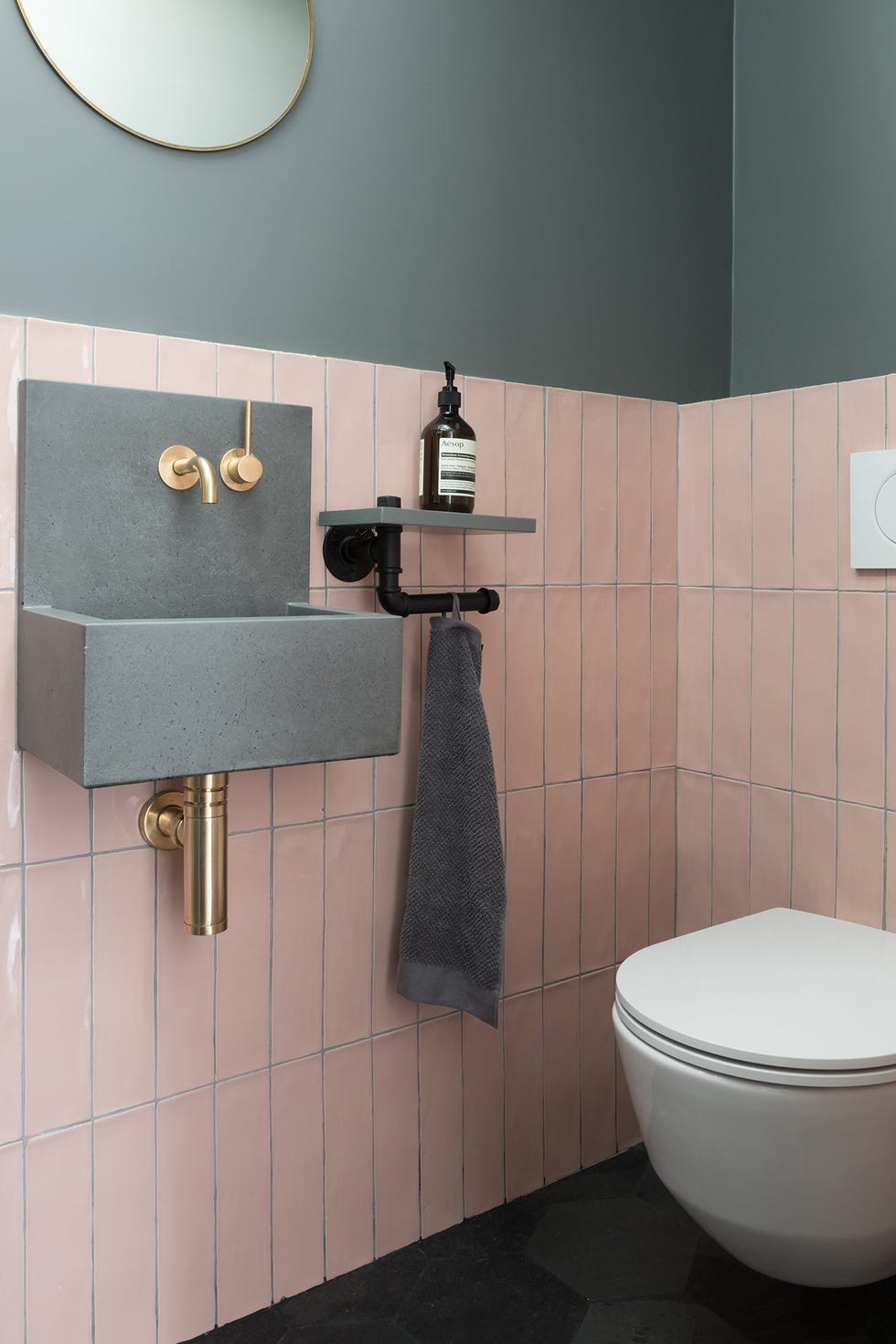 aseo de estilo industrial con pared a dos colores, azulejos en rosa empolvado, lavamanos flotante gris y grifería dorada