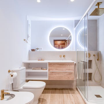 baño con ducha, mueble en blanco y madera volado, espejo redondo y griferías y detalles dorados