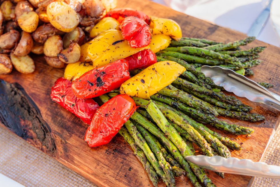 abundant platter of grilled and roasted asparagus, red and yellow peppers, and roasted potatoes  chef prepared and presented on a rustic wooden slab at an outdoor gathering at an event in washago, on, canada, july 22, 2019