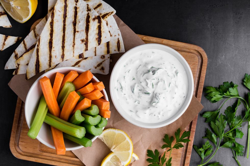 yogurt sauce with parsley and lemon juice served on rustic wooden board with pita bread and  fresh carrot and celery sticks