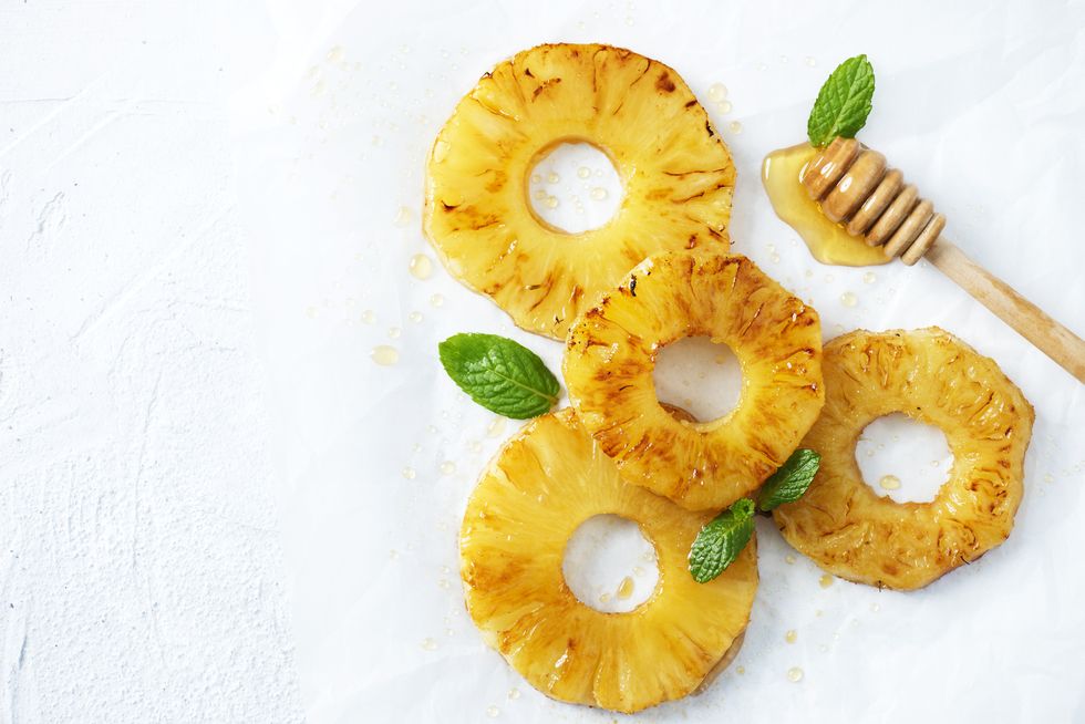 grilled pineapple with honey and mint leafs on white background