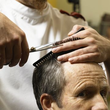 barber cutting senior man's hair, closeup of hands