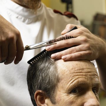 barber cutting senior man's hair, closeup of hands