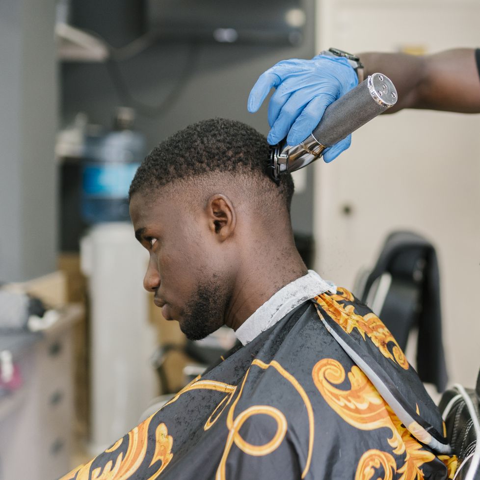 barber with locs wearing mask and glove while cutting customer's hair in salon