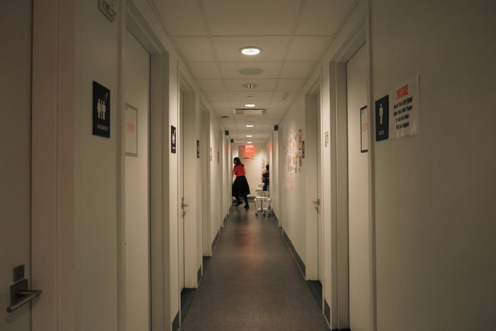 narrow hallway with multiple doors restroom signs and a person walking