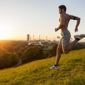 barechested man running on meadow in park at sunset