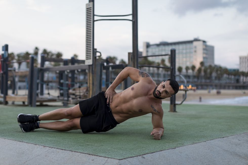 barechested muscular man doing side planks outdoors