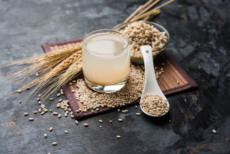 barley water in glass with raw and cooked pearl barley wheatseeds selective focus