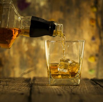 barman pouring whiskey in front of whiskey glass and bottles on black table with whiskey and ice on a glass table